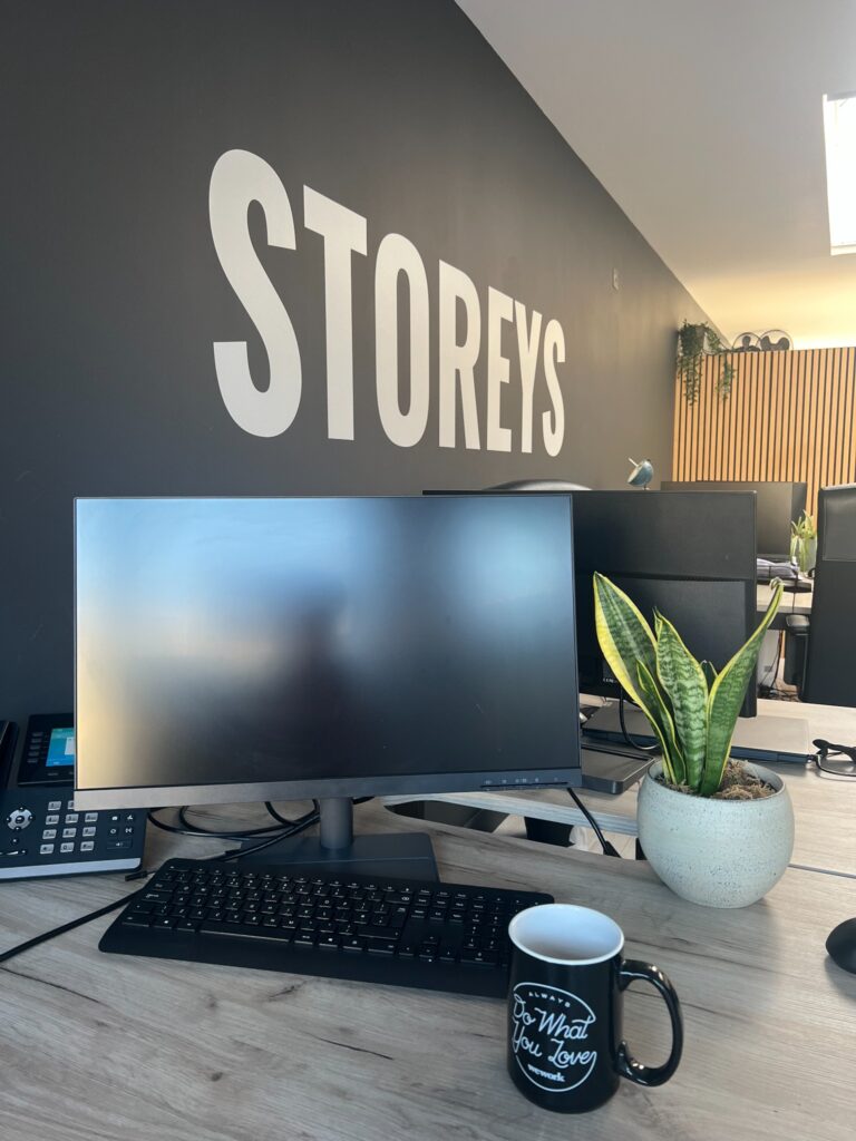 Modern office workspace with computer monitor, desk plant and Storeys wall branding